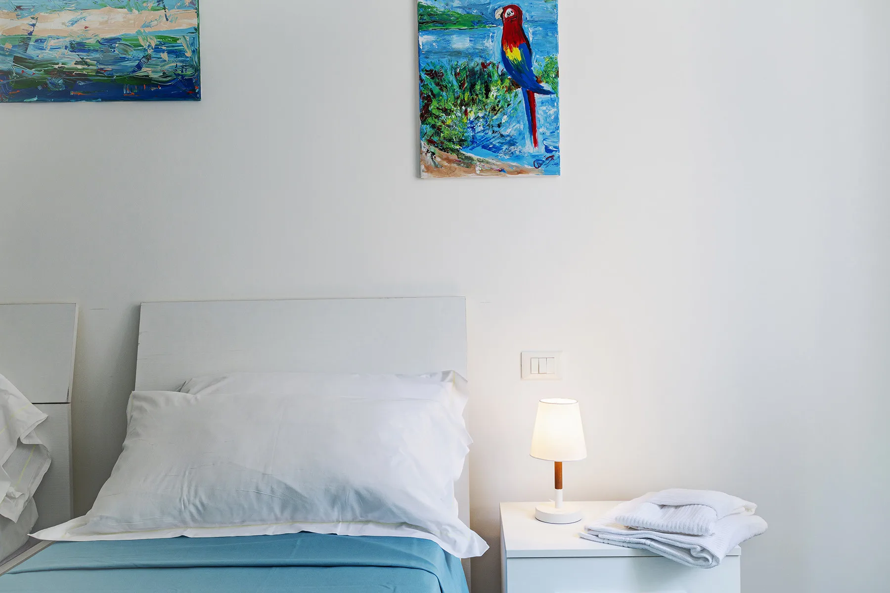 A bedroom with a neatly made bed and colorful artwork on the wall.