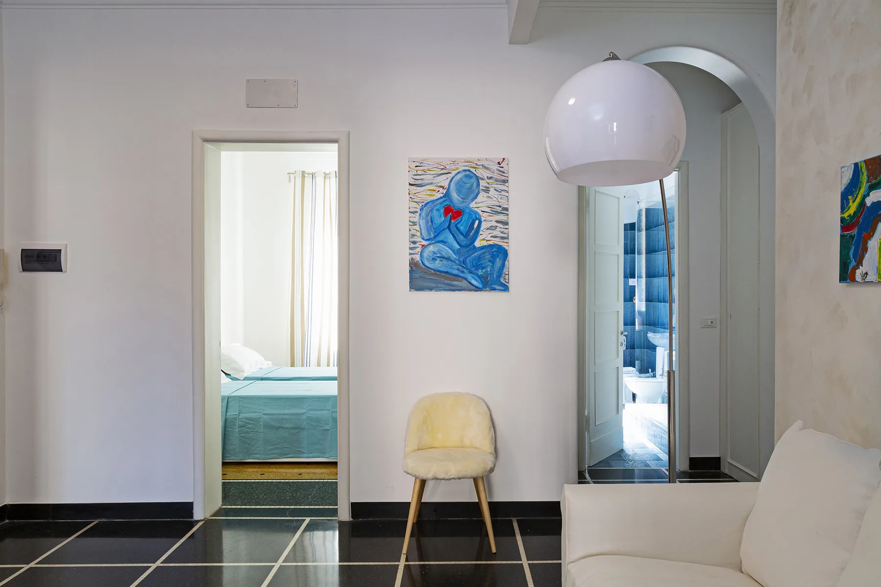 A bright bedroom with a bed, a chair, and colorful artwork on the walls.