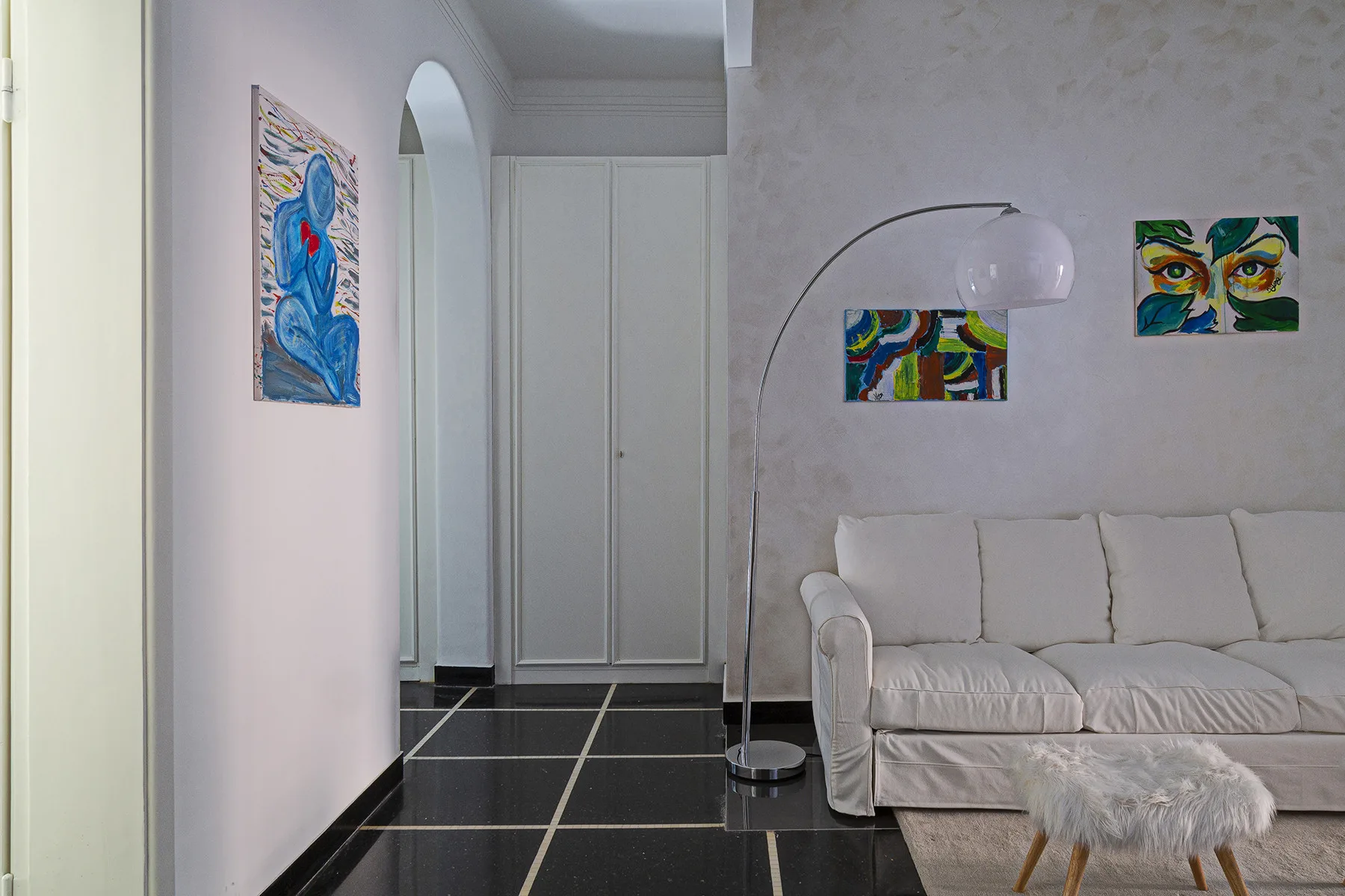 A bright living room with white seating and colorful artwork on the walls.