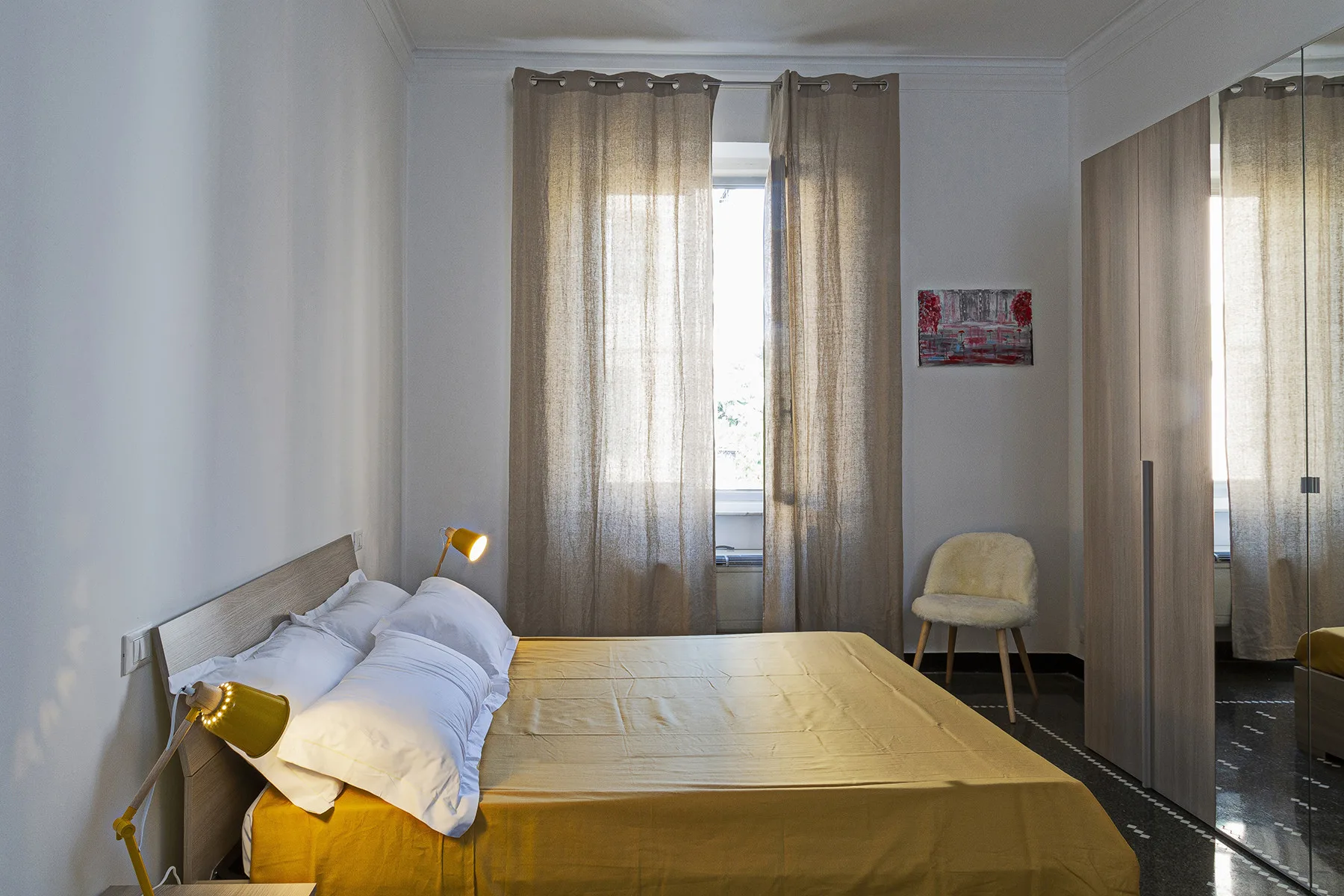 A bedroom with a bed beside a window covered by curtains.