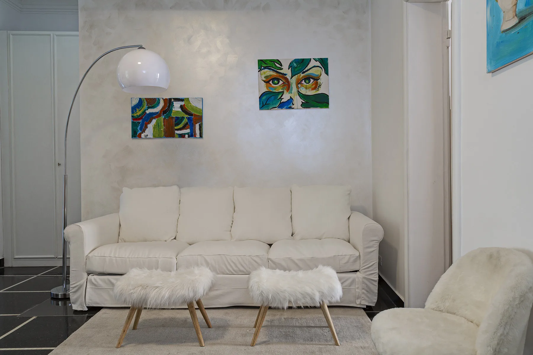 A living room with a sofa, two small tables, and colorful wall art.