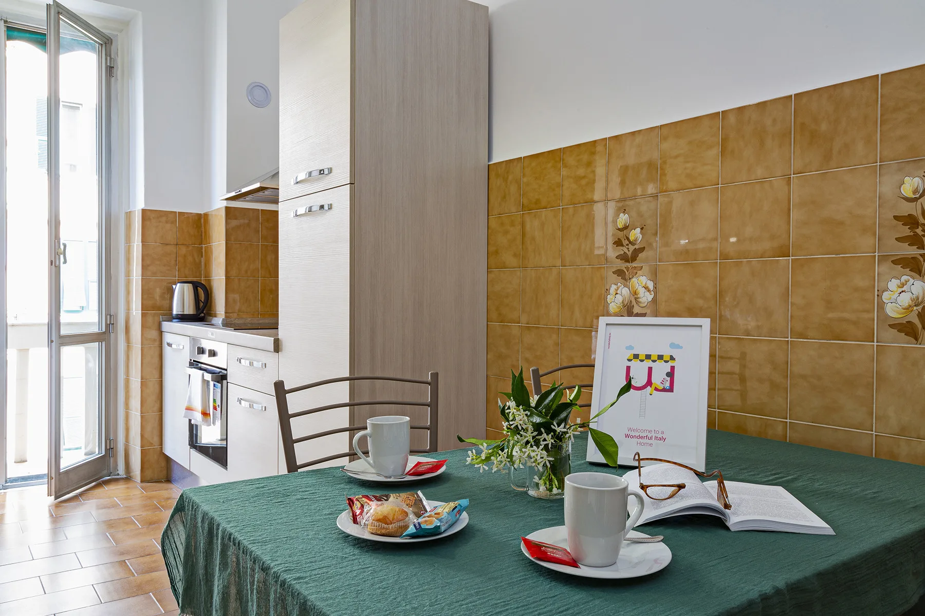 A bright kitchen with a green-covered table set with cups and plates.