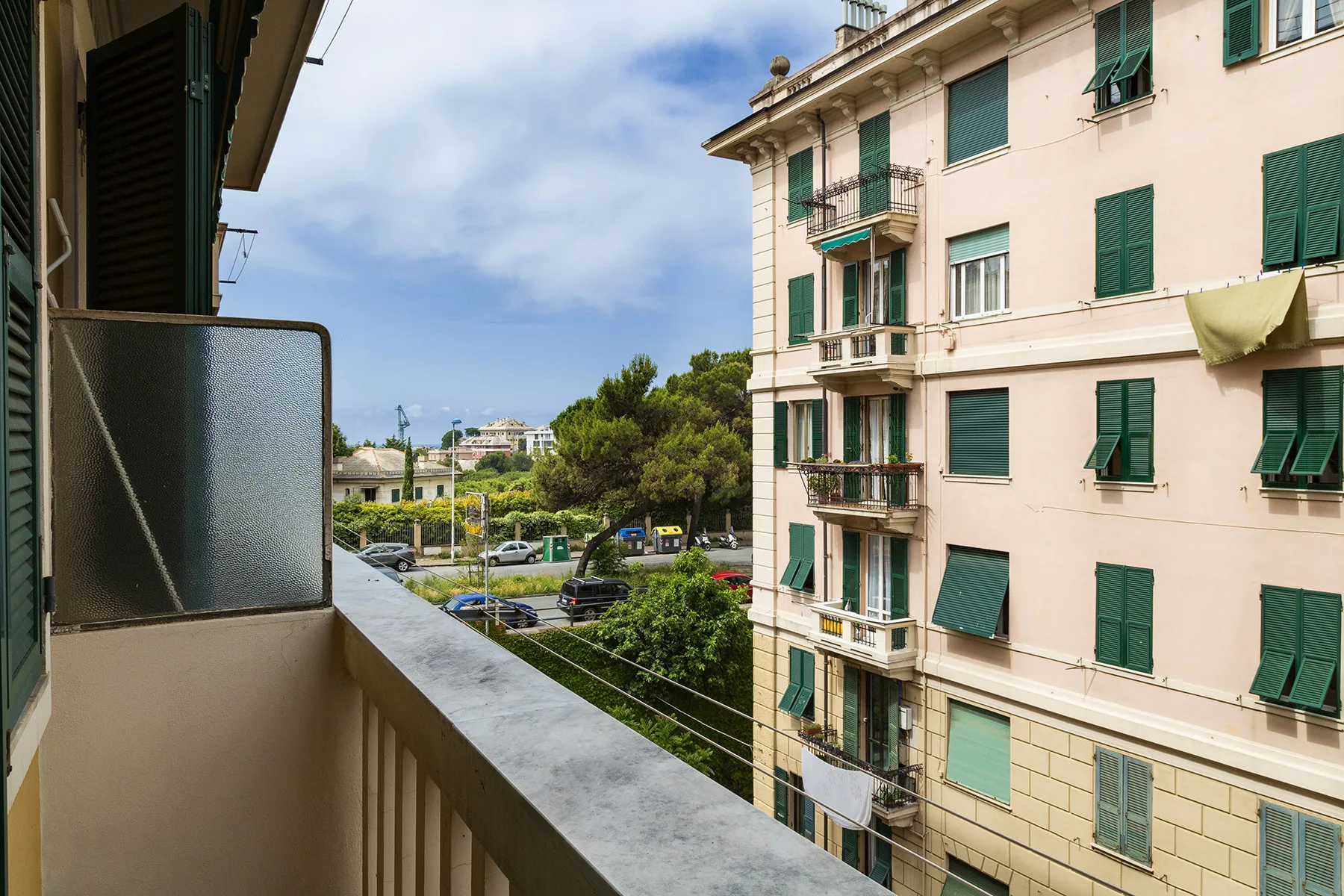 A balcony overlooks a tree-lined street and a neighboring apartment building.