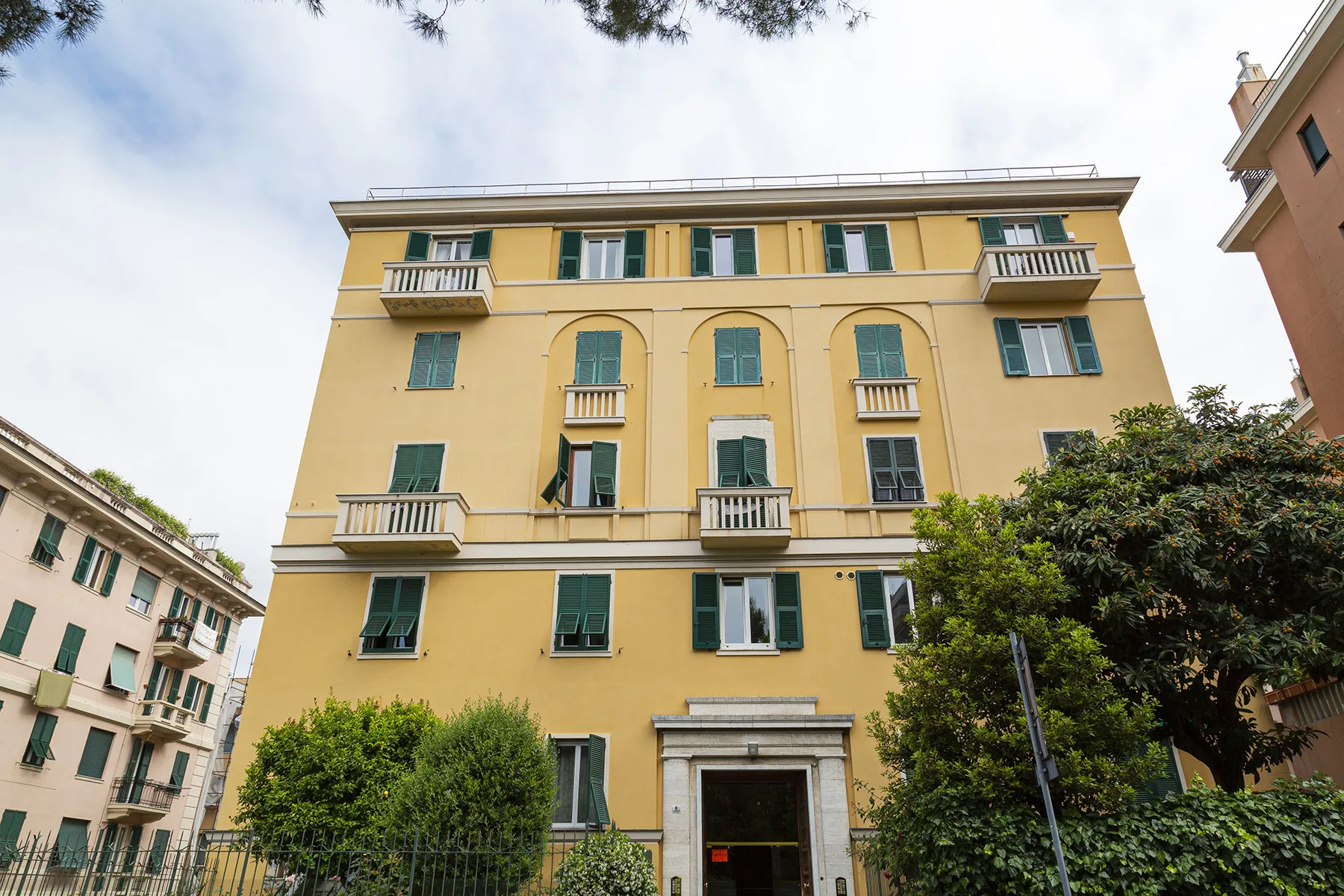 A yellow multi-story building stands behind leafy trees on a city street.