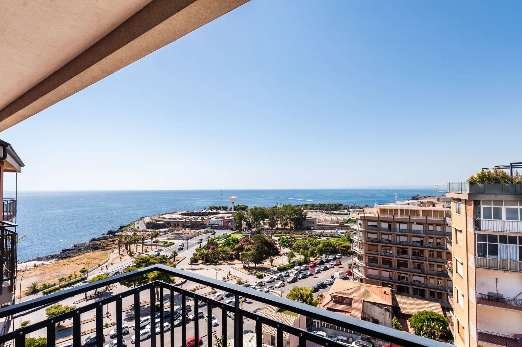 A balcony overlooks the sea, with nearby buildings and a landscaped coastal area.