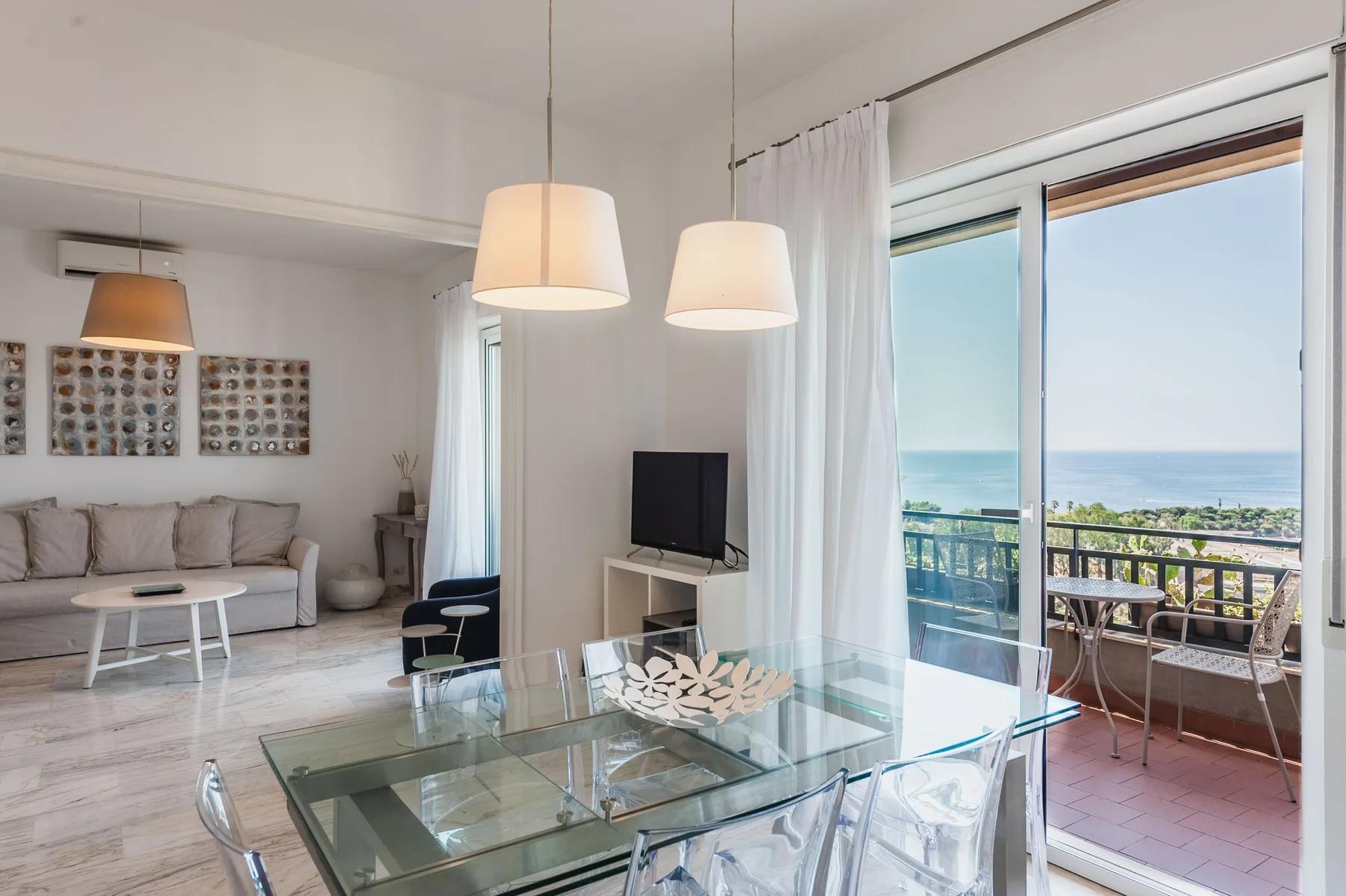 A bright living and dining area opens onto a balcony with an ocean view.