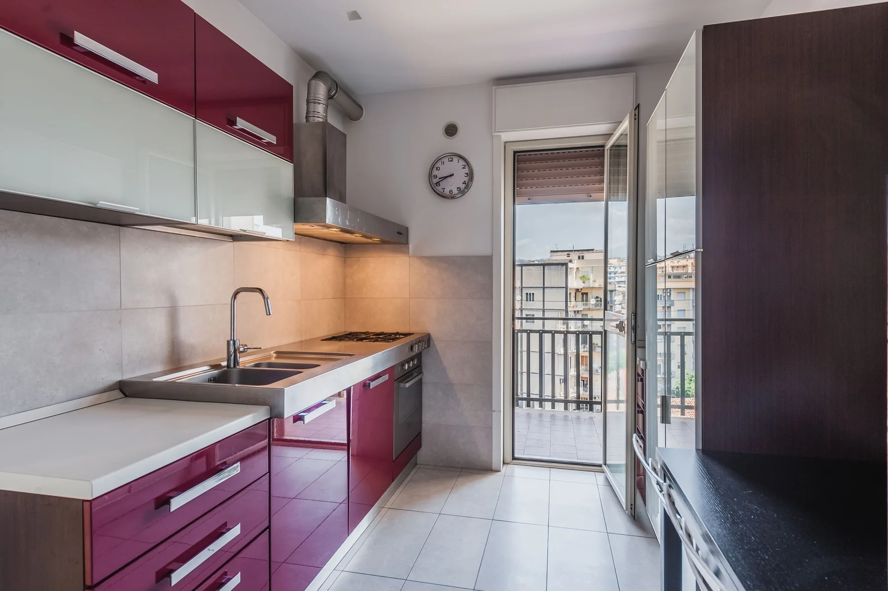 A modern kitchen with burgundy cabinets and a balcony door.