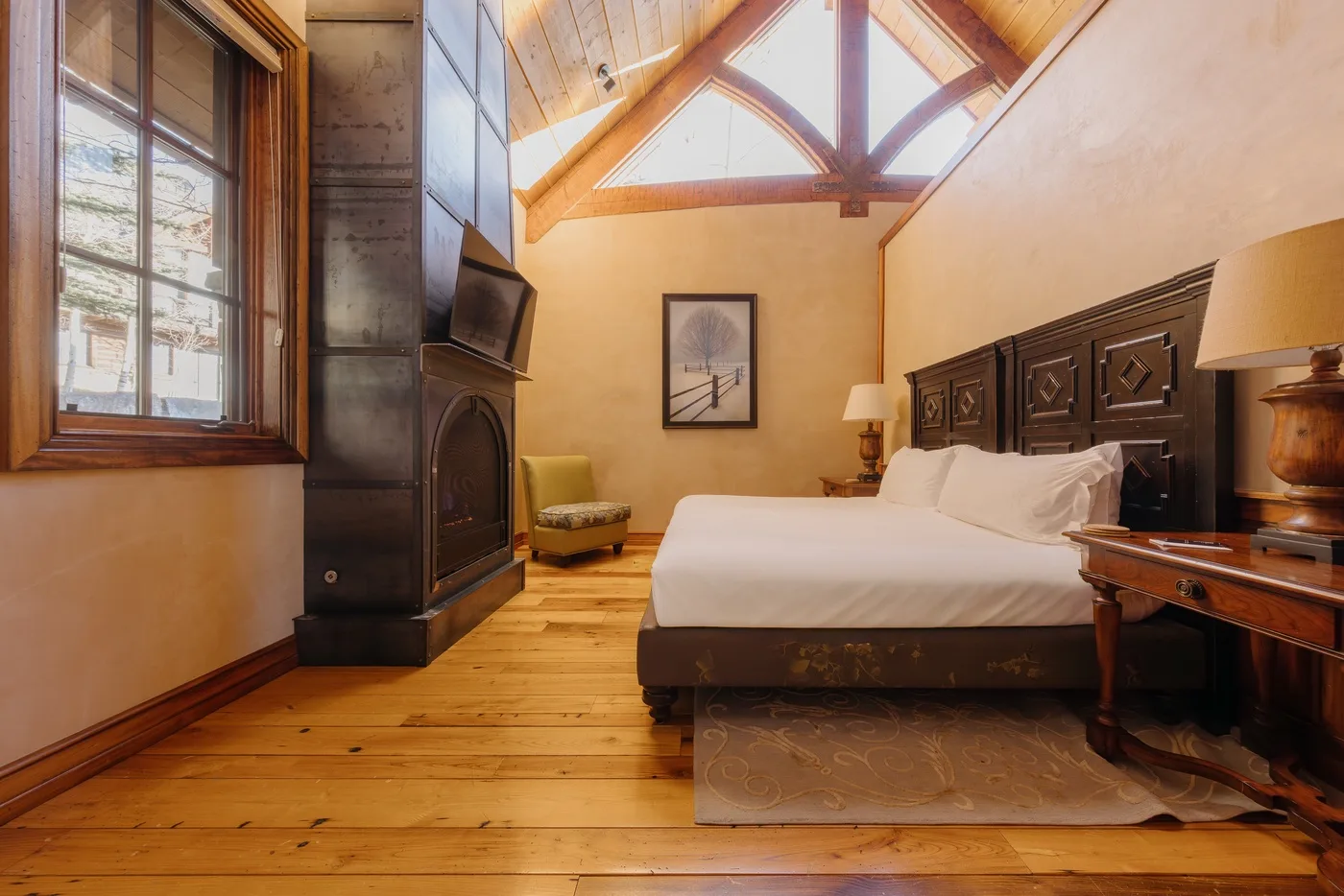 Un dormitorio con una cama grande, techo revestido de madera y ventanas altas.