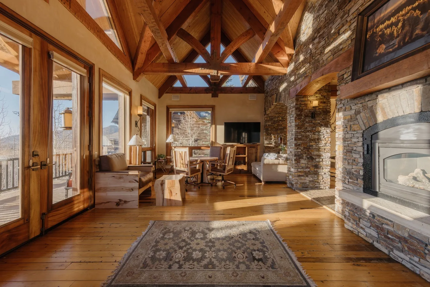 A rustic living room with exposed timber beams, stone walls, and a fireplace.