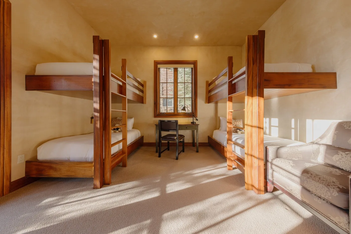 Un dormitorio con literas de madera, un escritorio bajo la ventana y asientos.