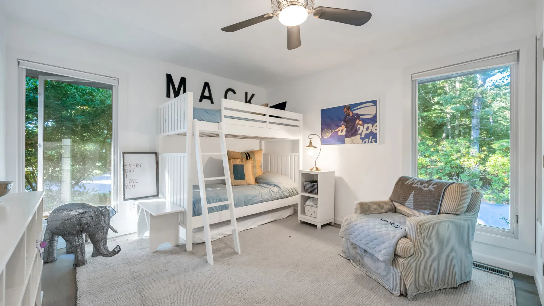 Un dormitorio luminoso con una litera blanca, un sillón y ventanas grandes.