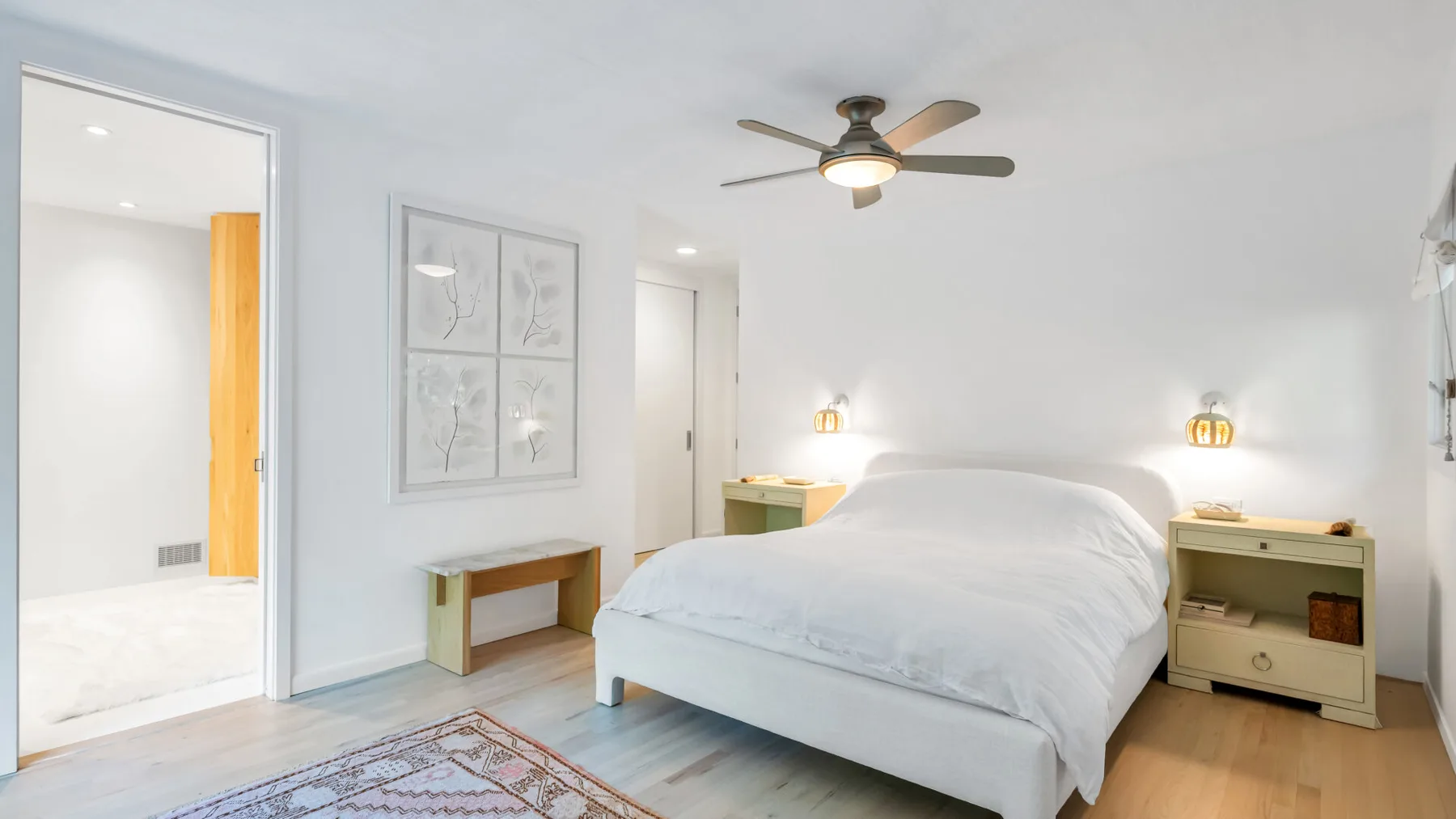 Un dormitorio luminoso con una cama bien tendida, mesitas de noche y un ventilador de techo.