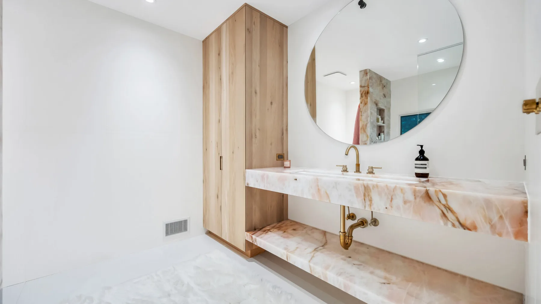 Un lavabo de baño con un espejo redondo grande y armarios de madera.