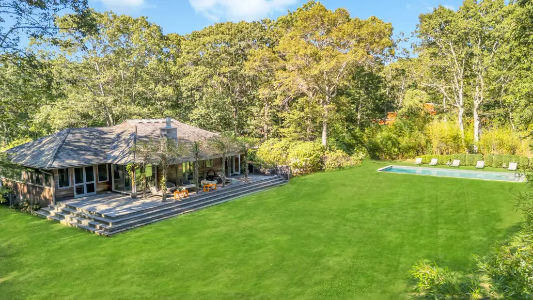A house and swimming pool sit beside a broad green lawn and trees.