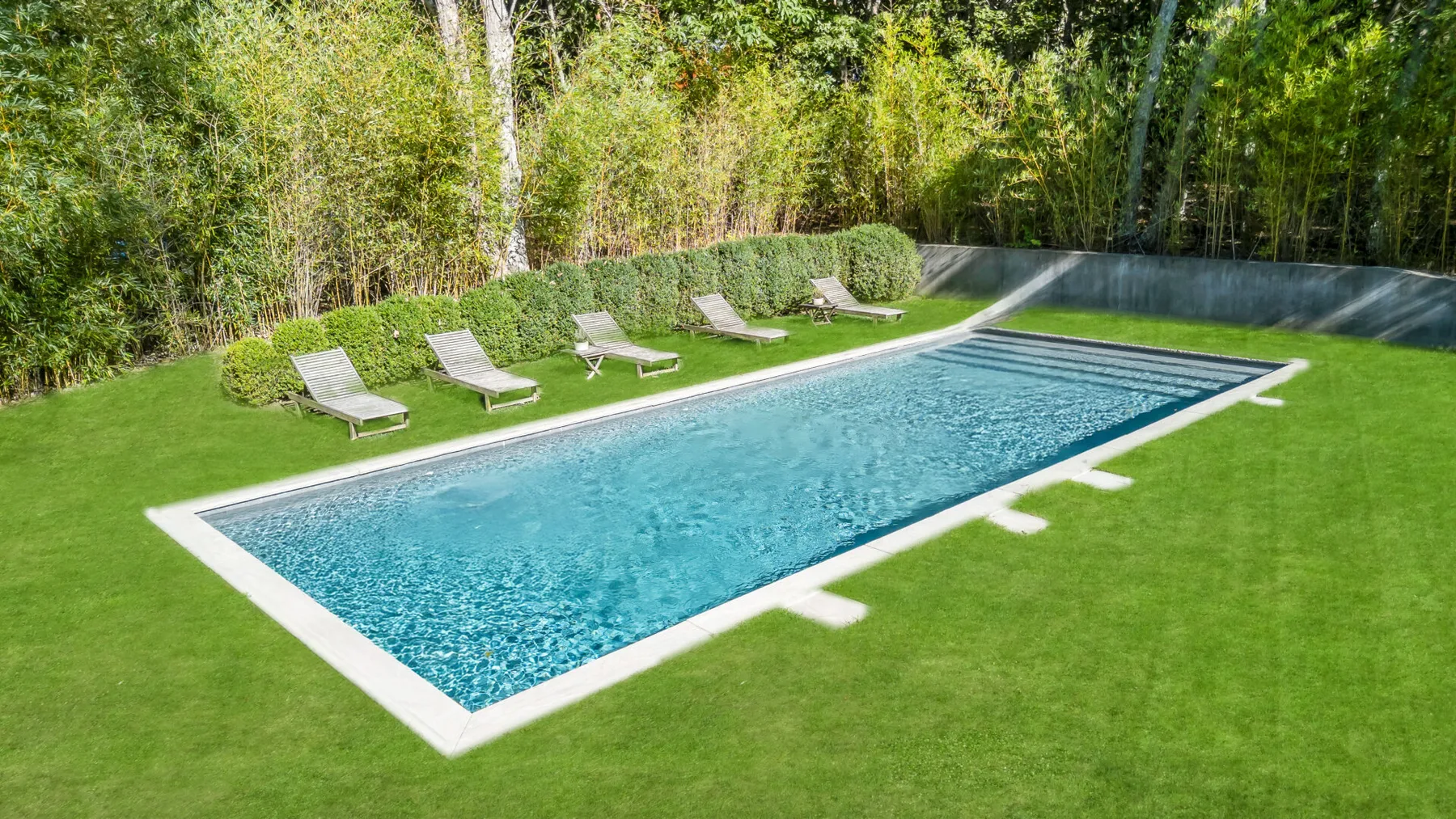 Una piscina rectangular está en un césped rodeado de vegetación.