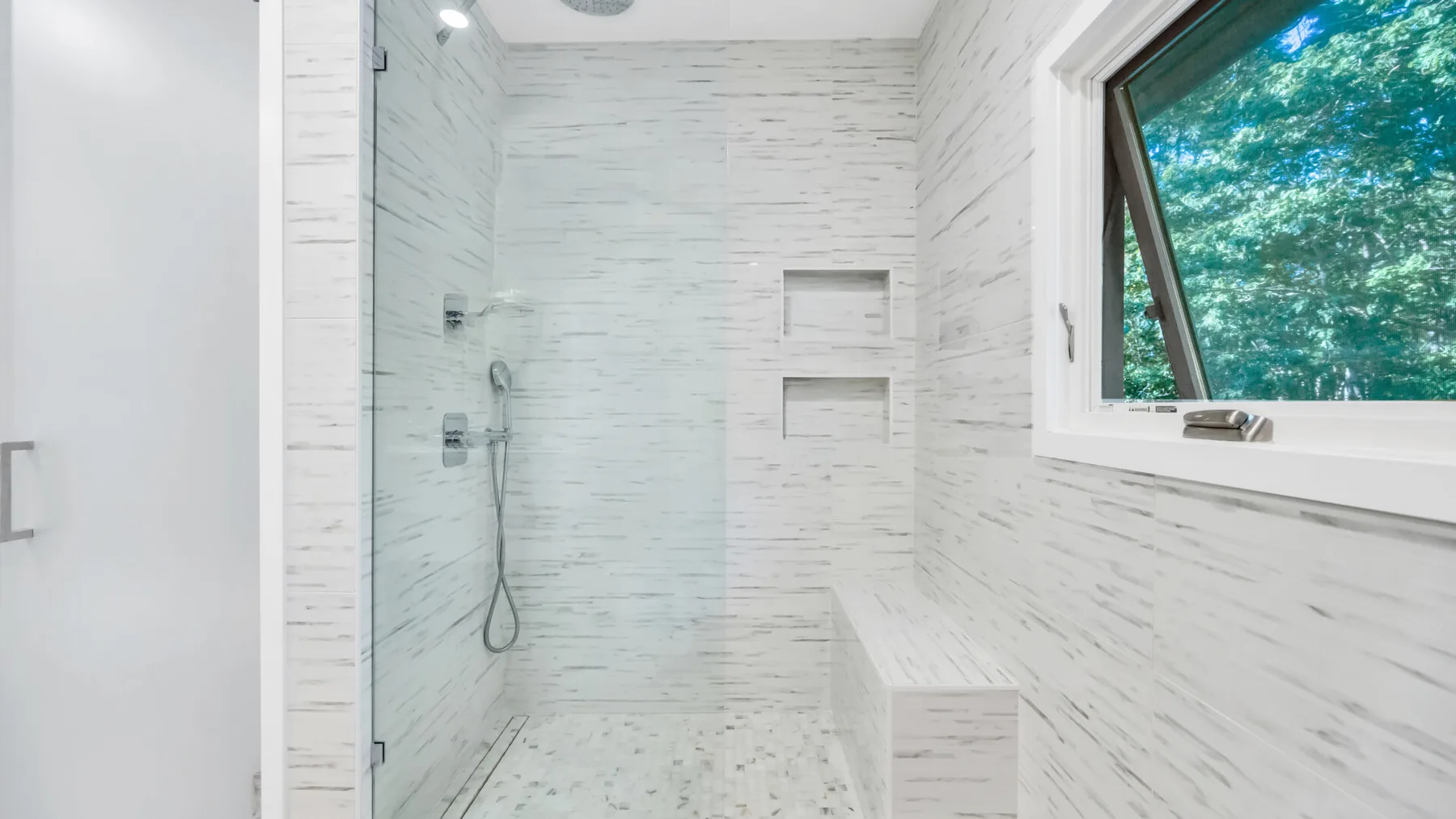 Un baño luminoso con ducha a ras de suelo y una ventana con vistas a los árboles.