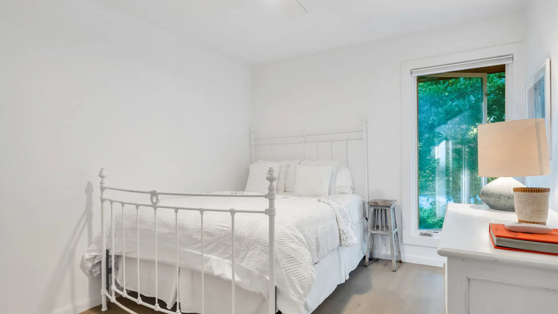 Un dormitorio luminoso con una cama blanca junto a una ventana grande.