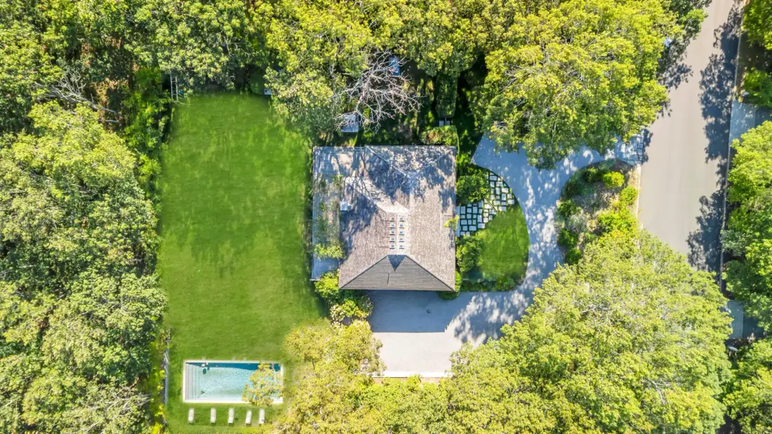 Una vista aérea muestra una casa rodeada de árboles, con césped y una piscina.