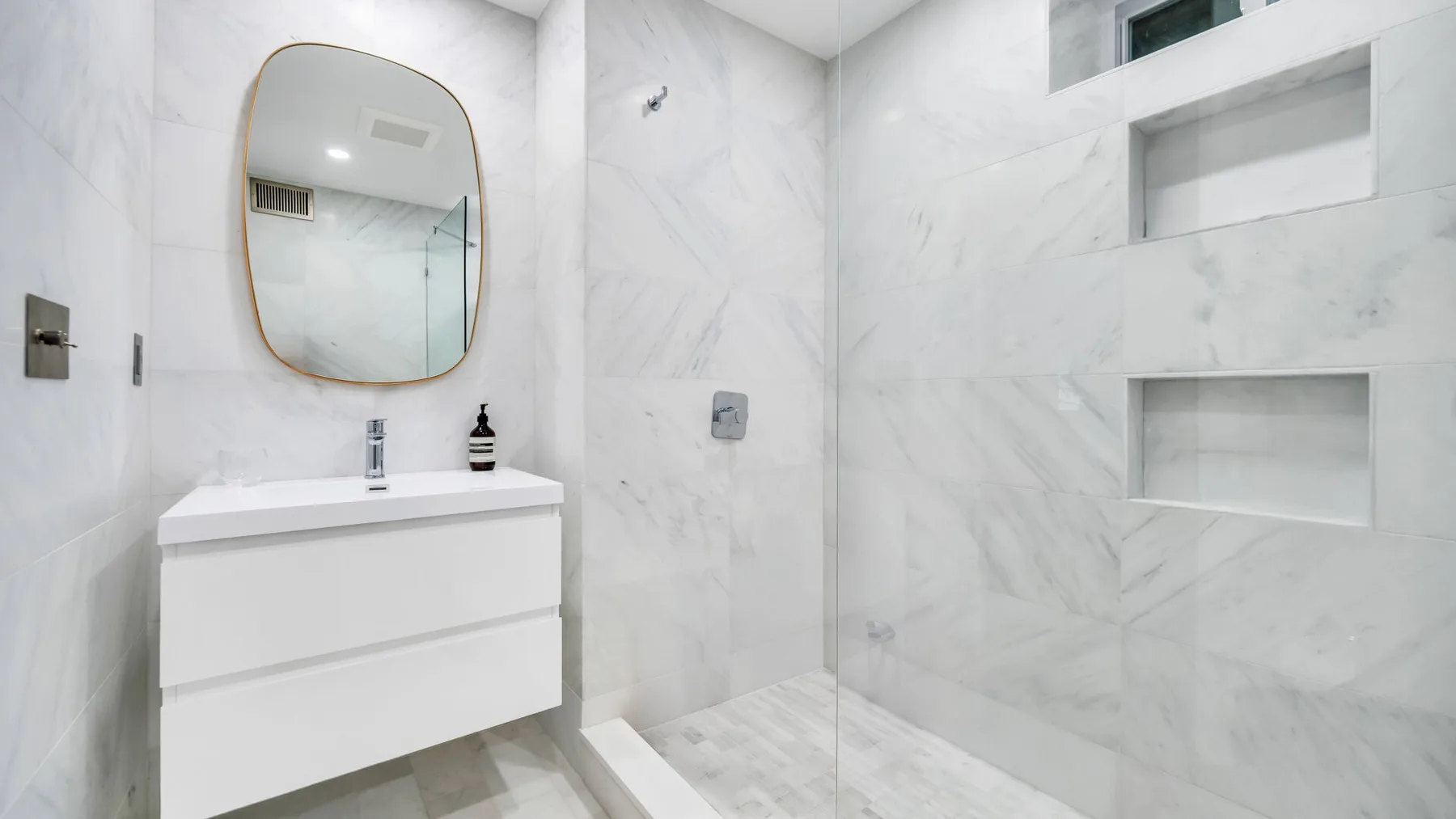 Un baño luminoso de mármol con un lavabo suspendido, espejo y nichos empotrados.