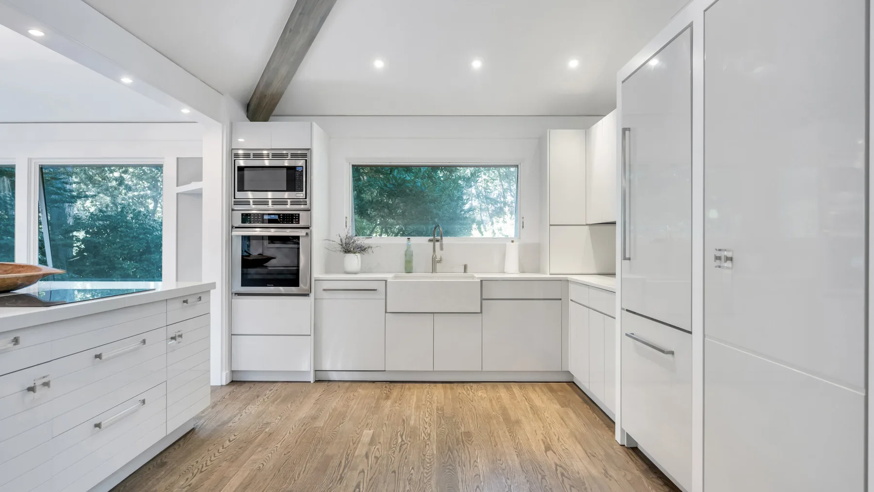 Una cocina moderna y luminosa con gabinetes blancos y una ventana amplia con vista a la vegetación.