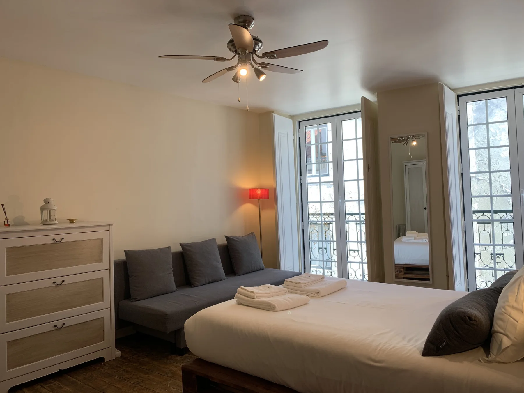 Un dormitorio con una cama bien hecha, asientos grises y ventanas altas.