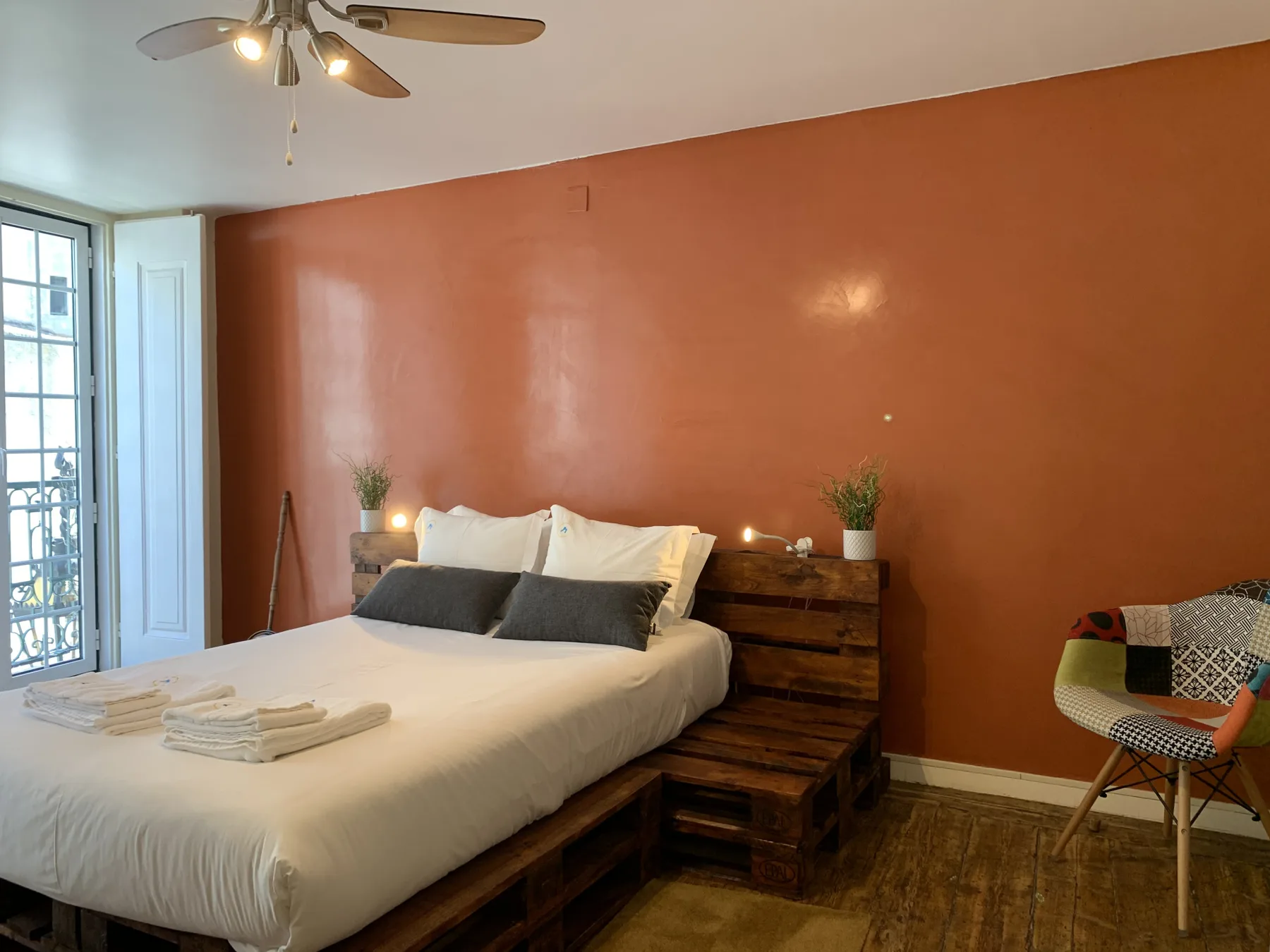 Un dormitorio con una cama blanca, muebles de madera junto a la cama y una silla estampada.