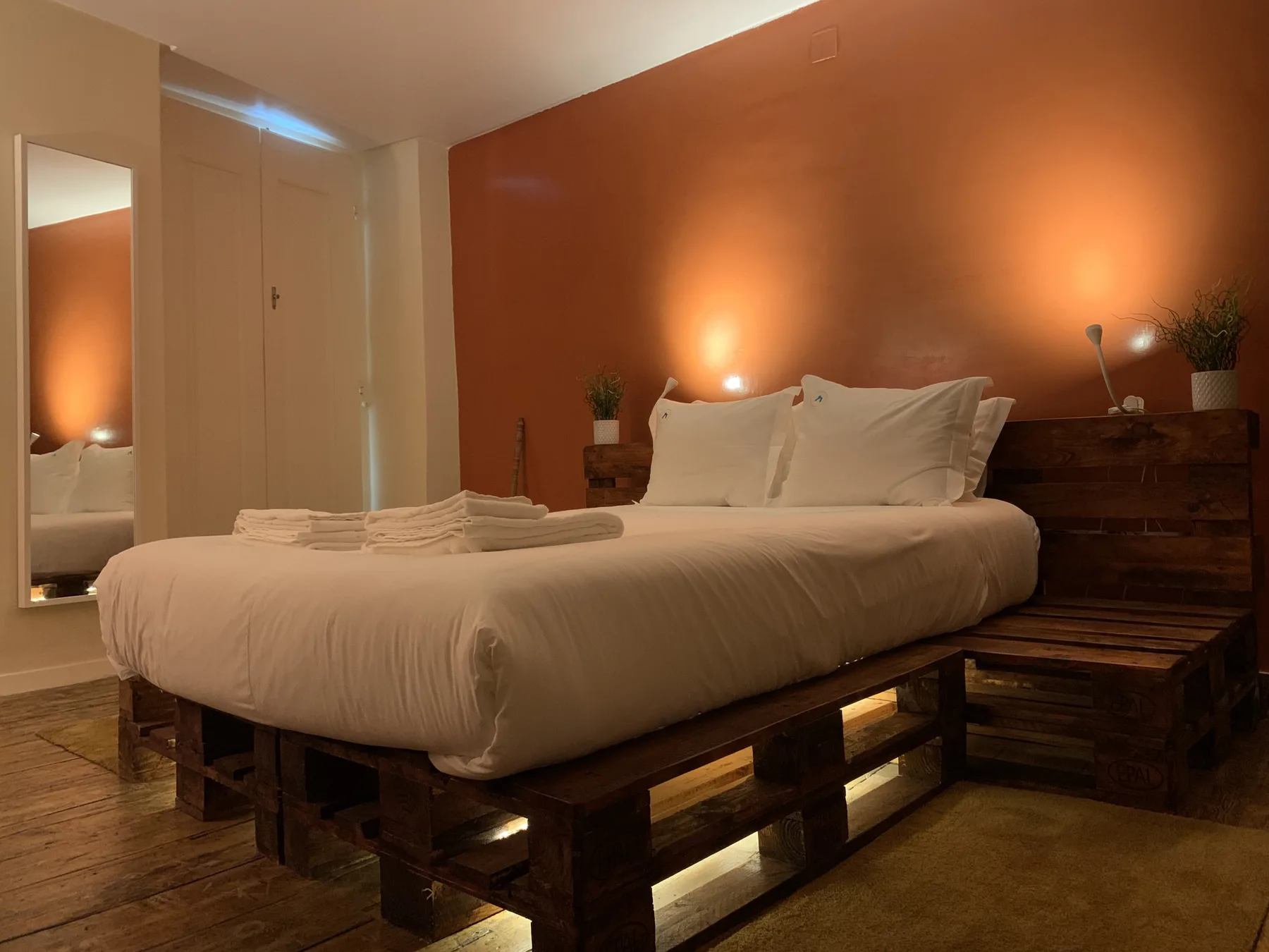 Dormitorio con una cama e iluminación cálida frente a una pared naranja.