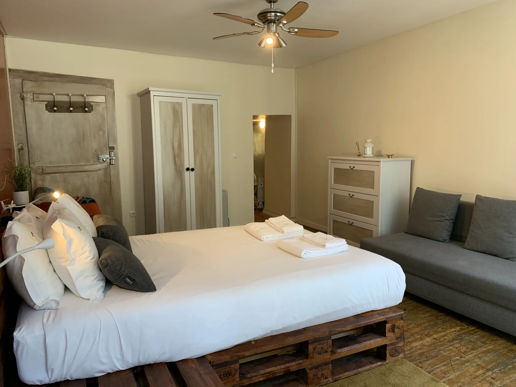 Un dormitorio con una cama grande, una zona de asientos gris y un ventilador de techo.