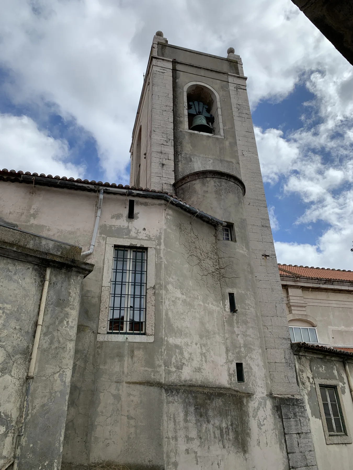 Una torre de campanario de piedra se alza sobre edificios contiguos bajo un cielo nublado.