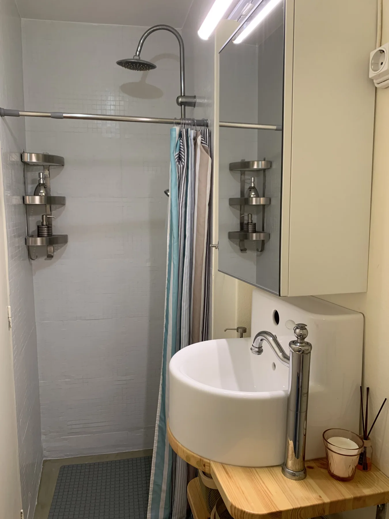 Un baño compacto con ducha, lavabo curvo y encimera de madera.