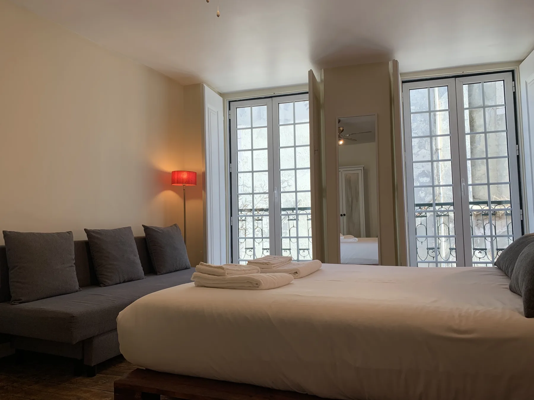 Dormitorio con una cama tendida, asientos oscuros y ventanas altas.
