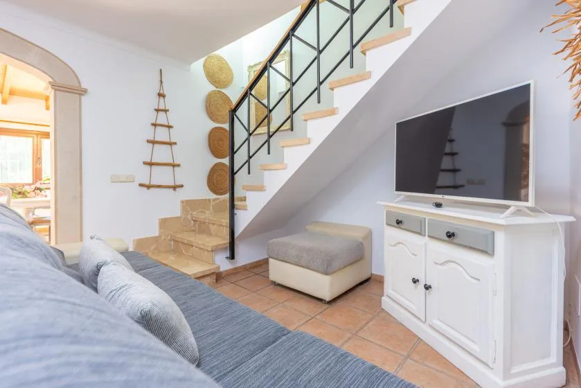 Una sala luminosa con un televisor bajo una escalera y asientos en primer plano.
