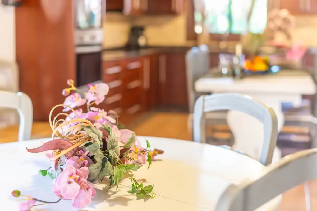 Una zona de comedor con un arreglo floral sobre la mesa y armarios de cocina detrás.
