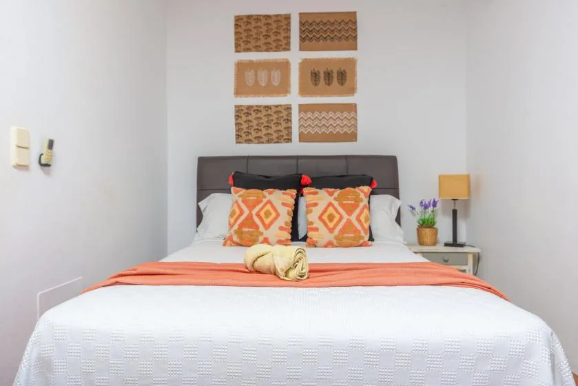 Un dormitorio con una cama bien tendida y almohadas estampadas de colores.