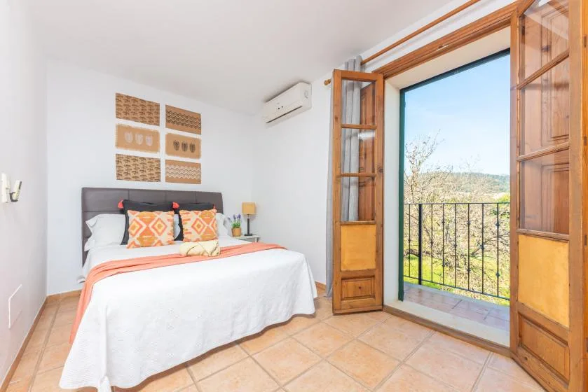 Un dormitorio con una cama junto a puertas de madera abiertas que dan a un balcón.