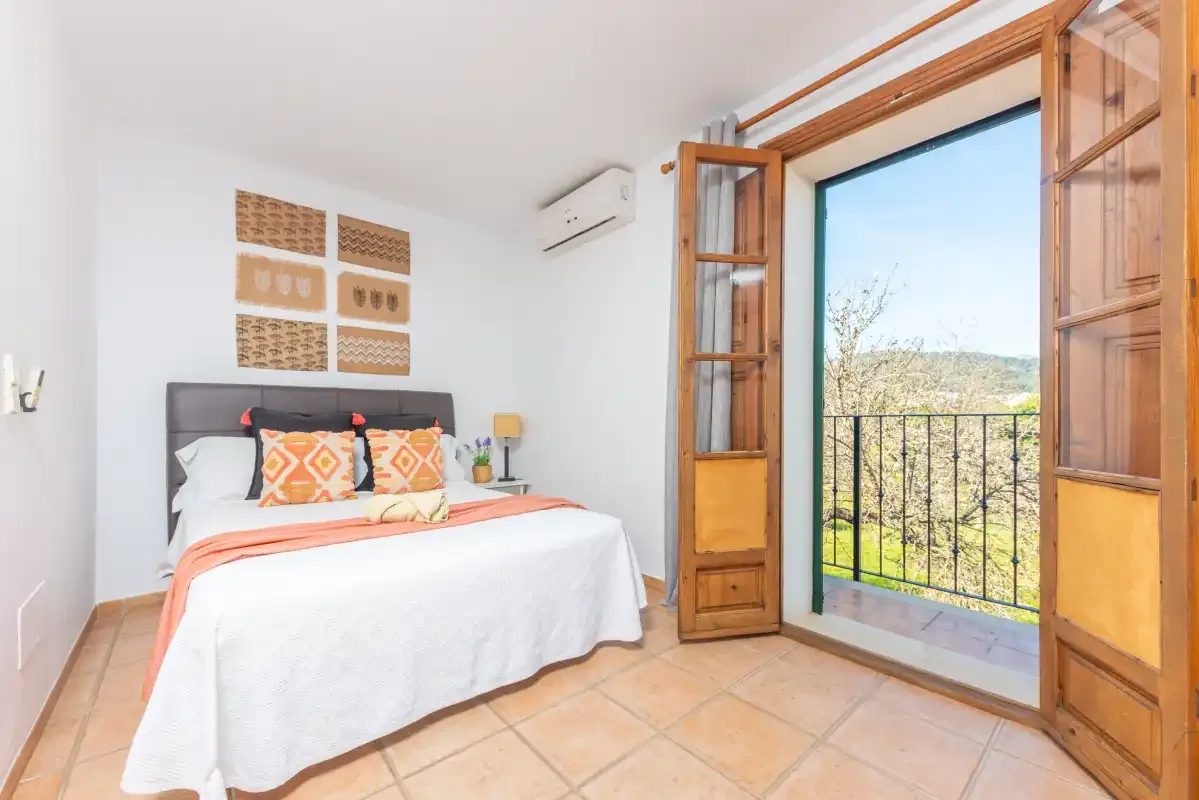 Un dormitorio con una cama doble junto a puertas de madera abiertas que dan a un balcón.