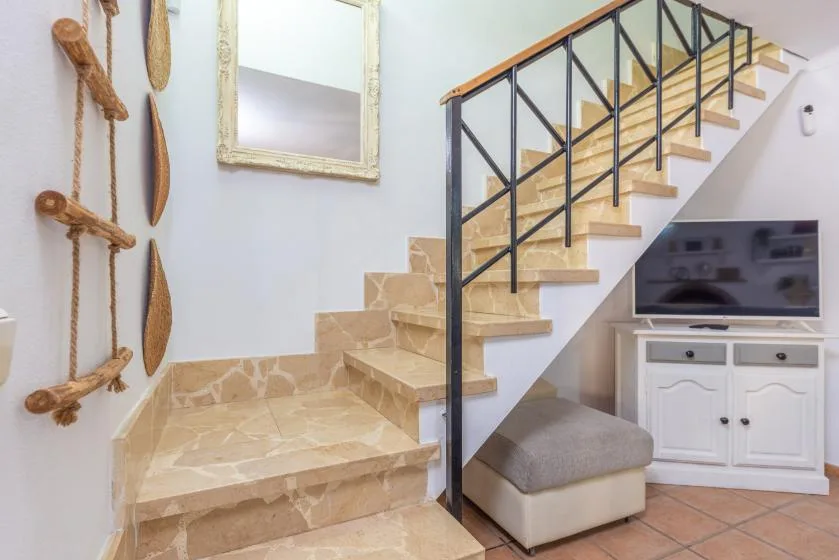 Una escalera de azulejos con barandilla negra sube junto a un mueble con televisor.