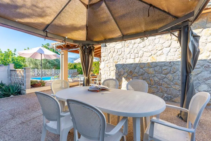 Un comedor exterior a la sombra, con mesa y asientos junto a un muro de piedra.