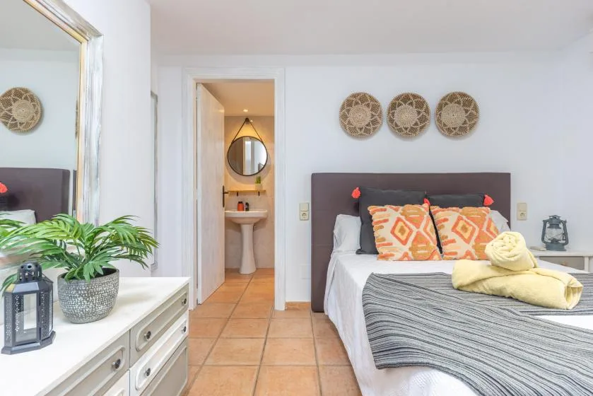 Un dormitorio luminoso con una cama tendida y una puerta abierta hacia el baño.