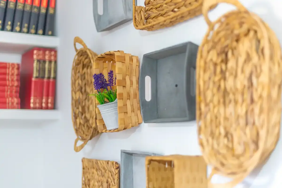 Una pared muestra cestas tejidas, libros y una pequeña planta en maceta.