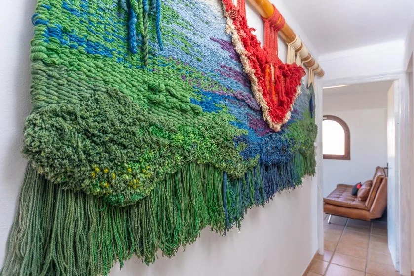 Un tapiz tejido de colores cubre la pared del pasillo, con asientos visibles en la habitación contigua.
