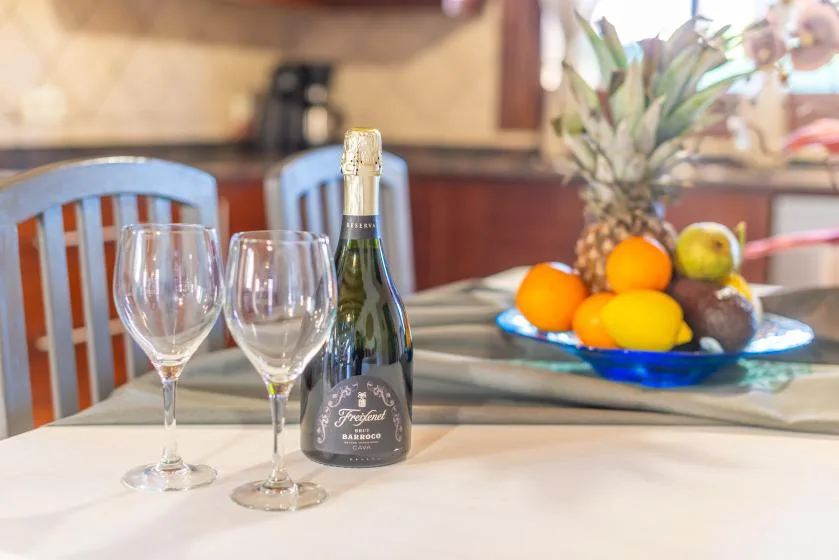 Una mesa de comedor con copas y una botella de vino, y un frutero detrás.