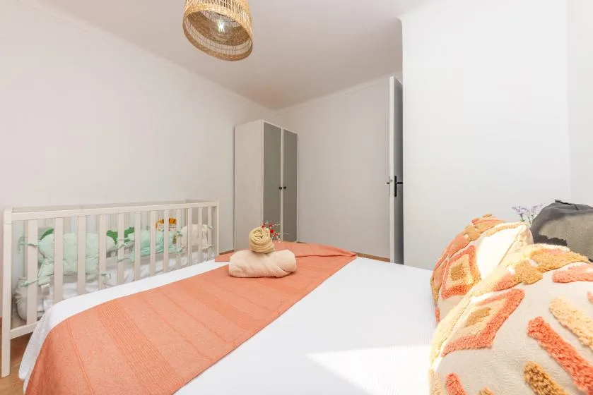 Un dormitorio luminoso con una cama, una cuna y un armario.