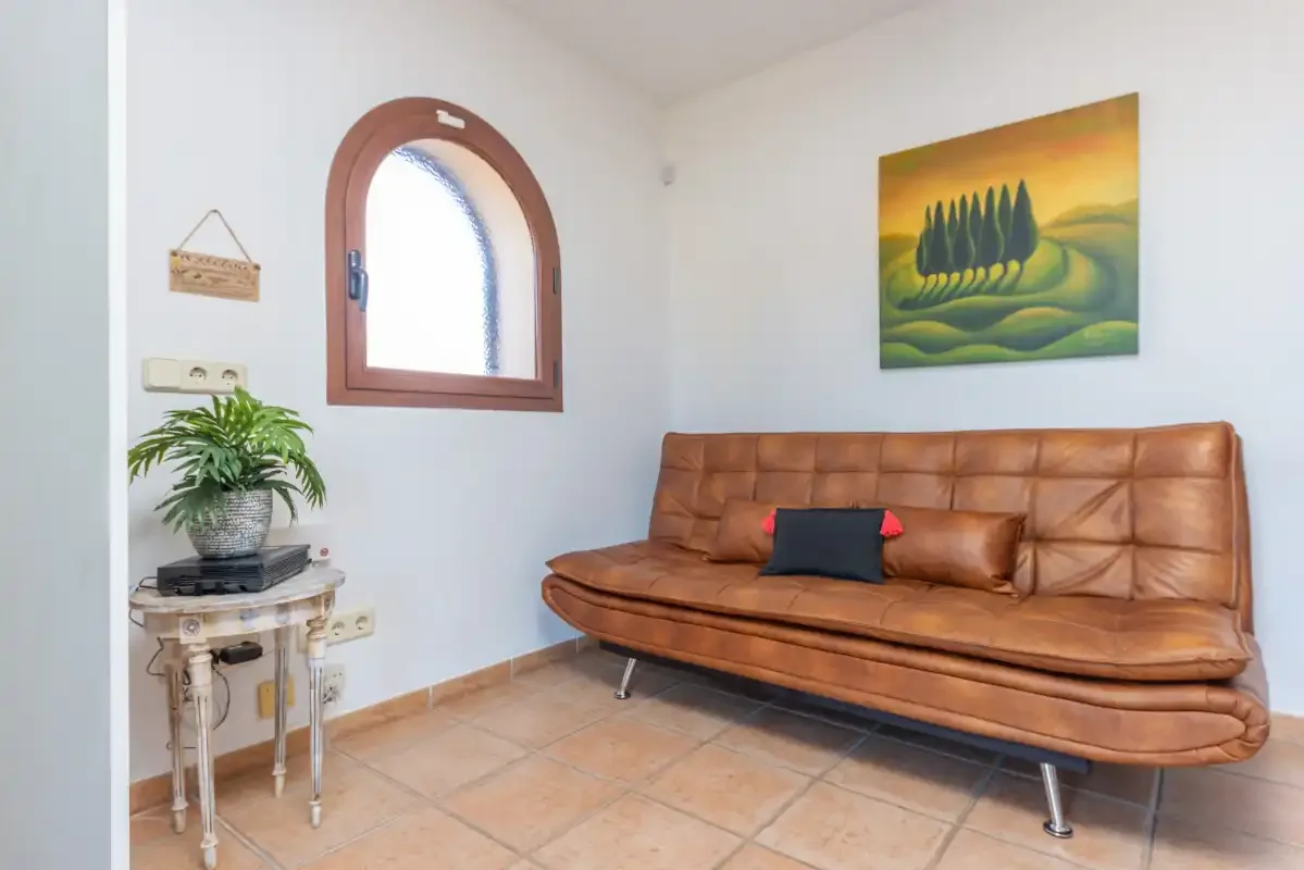 Una zona de estar con un sofá marrón bajo una pintura de paisaje.