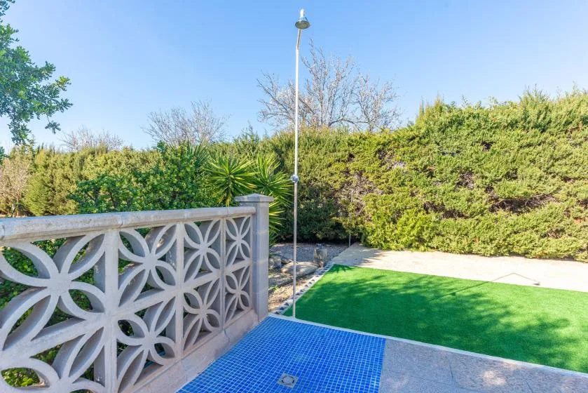Un patio exterior con una zona de baldosas azules, césped verde y setos alrededor.