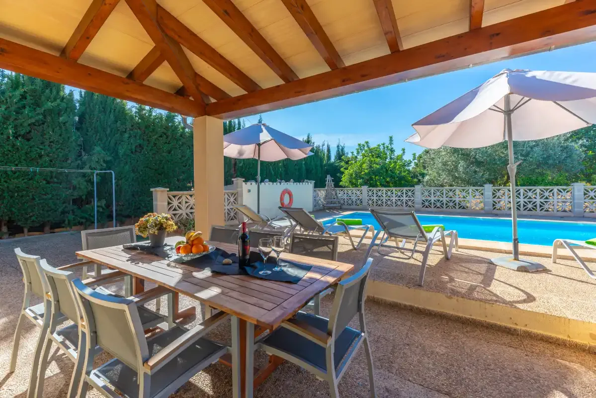 Una zona cubierta de comedor al aire libre da a una piscina y tumbonas.