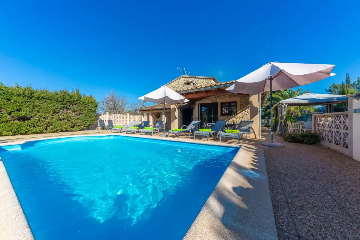 Una piscina al aire libre está junto a un patio con asientos y sombrillas.