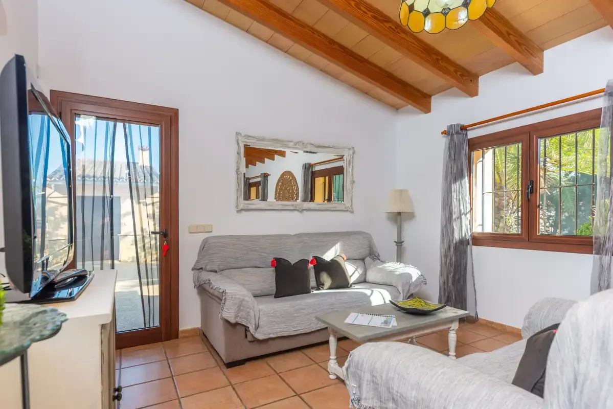 Una sala de estar con asientos, una mesa de centro y ventanas bajo un techo con vigas de madera.