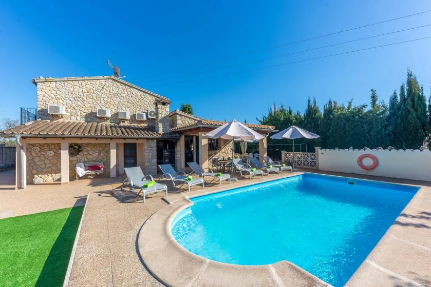 A swimming pool sits beside a stone building with lounge seating.