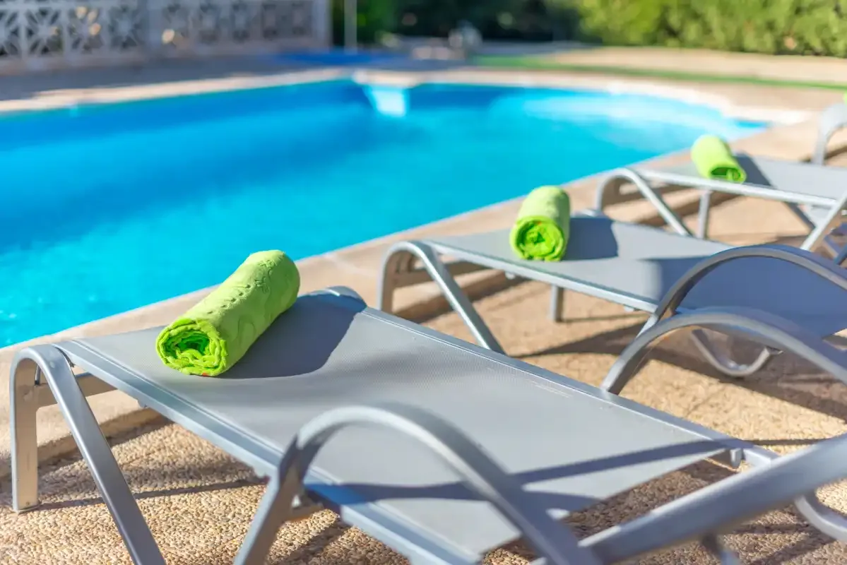 Tumbonas con toallas enrolladas están junto a una piscina azul.